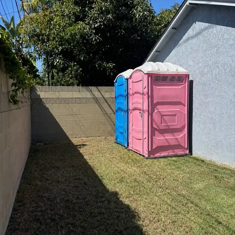 Two event portable toilets set along a fence in a backyard
