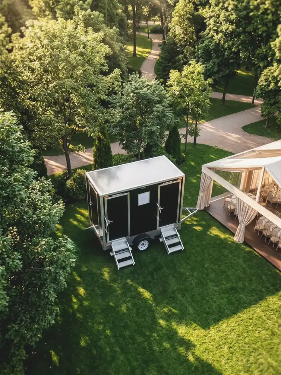 Restroom trailer parked on a lawn beside a backyard wedding tent
