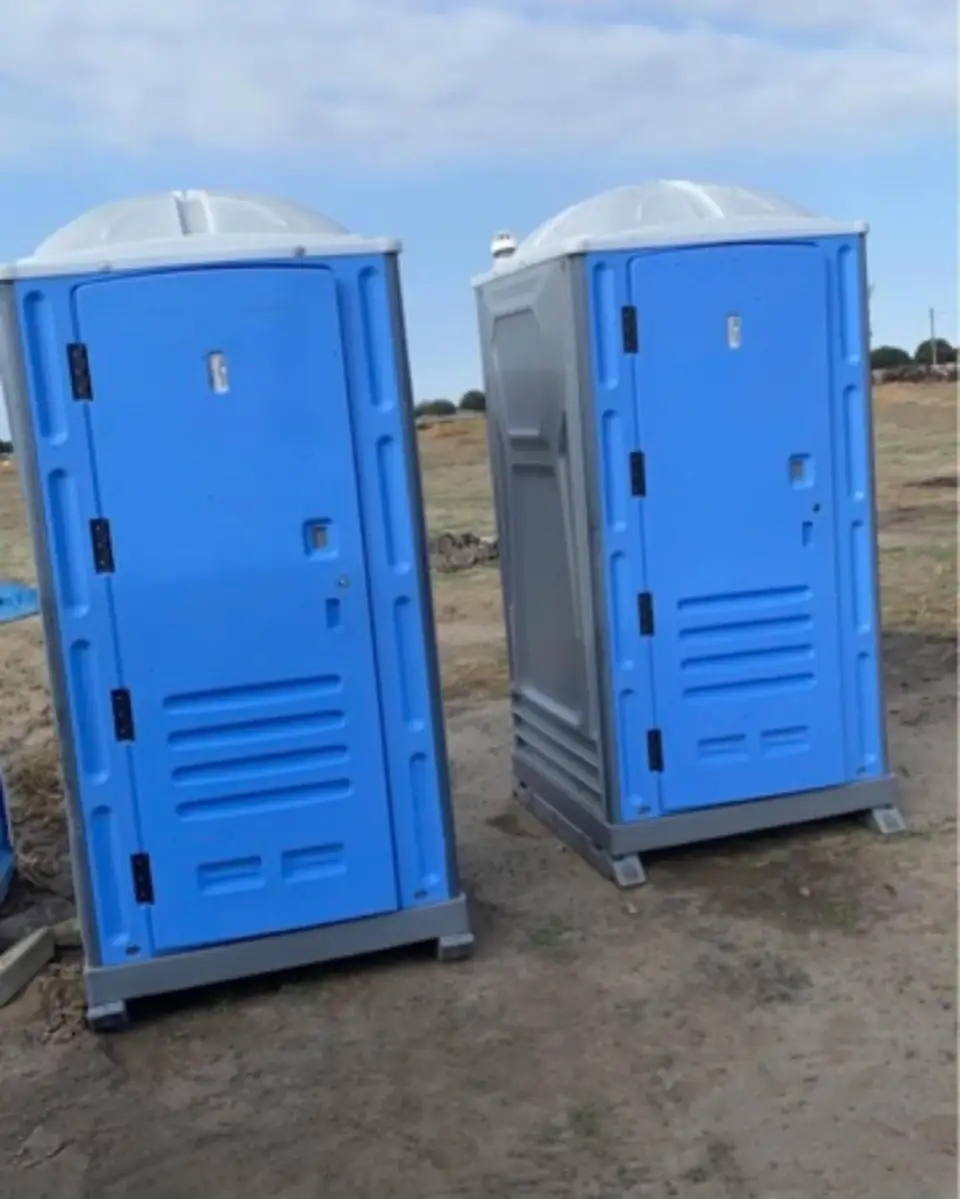 Two standard portable toilets on a graded dirt job site